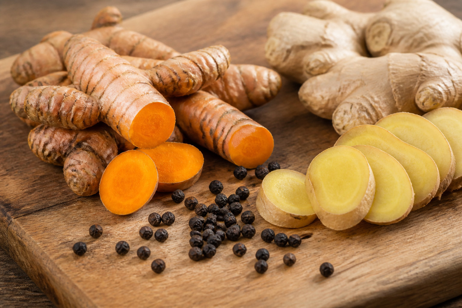 Racines de curcuma, gingembre frais en tranches et grains de poivre noir sur une planche en bois